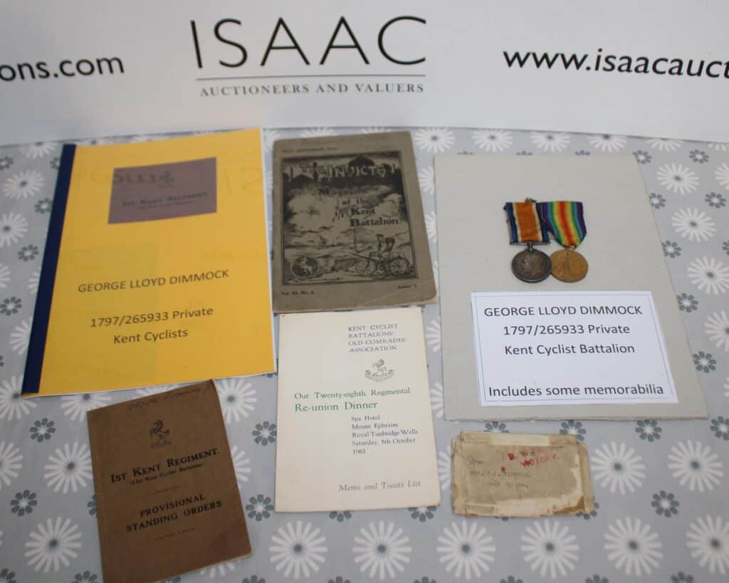 A collection of military memorabilia for Private George Lloyd Dimmock, including medals, documents, a regimental booklet, and a reunion dinner menu, displayed on a patterned surface.